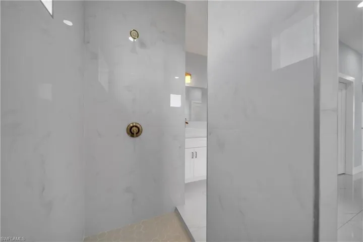 Walk-in shower with large format white tile walls, bronze-finish fixtures, and a honeycomb-patterned floor