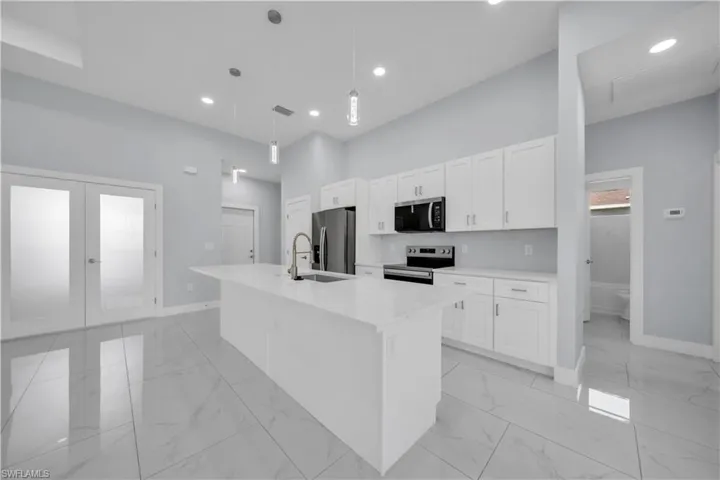 Spacious kitchen featuring an expansive island with a sink, stainless steel appliances, white shaker cabinetry, and light-toned tile flooring