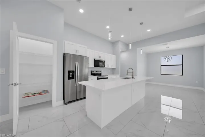 Modern kitchen featuring a large island with sink, white shaker cabinetry, stainless steel appliances, and white stone countertops