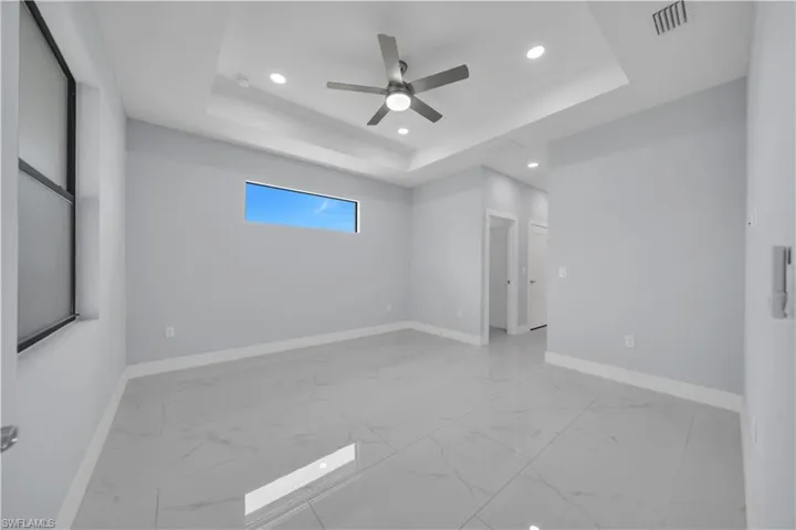 Spacious room featuring large format tile flooring, a tray ceiling with recessed lighting, a ceiling fan, and a horizontal window