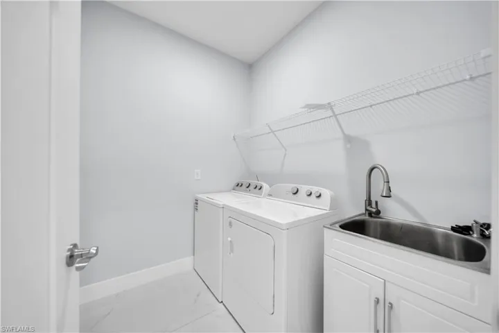 Dedicated utility space featuring a laundry sink with a gooseneck faucet, white base cabinetry, and overhead wire shelving