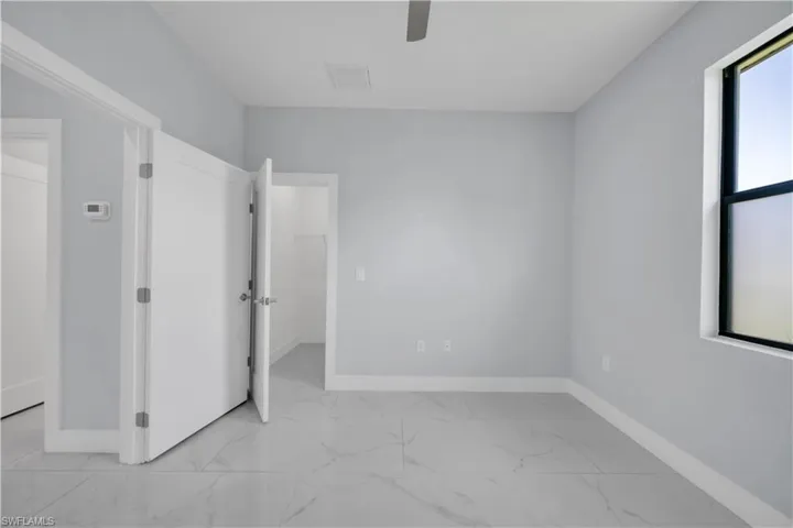 Bright room with light gray walls, large format tile flooring, a window with a black frame, and white paneled doors
