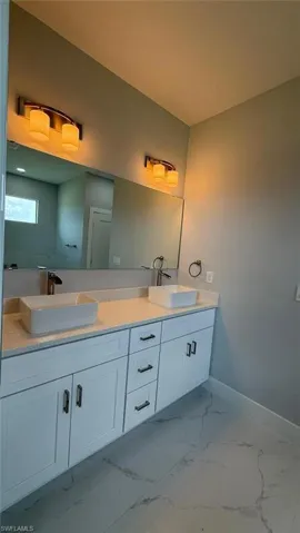 Bathroom with double vanity and light marble finish flooring