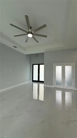 Unfurnished room featuring french doors, a raised ceiling, and light marble finish flooring