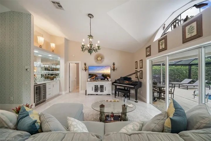 Tiled living room featuring a notable chandelier, wine cooler, and vaulted ceiling