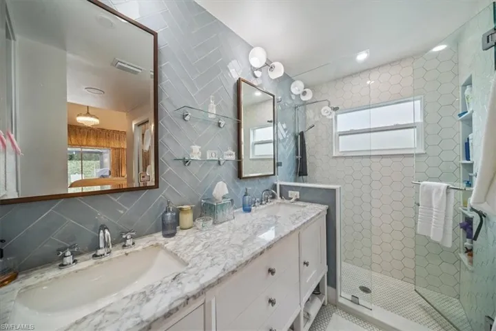 Bathroom with tile walls, walk in shower, backsplash, and dual bowl vanity