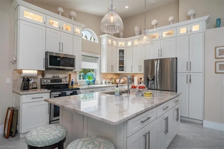 Kitchen featuring hanging light fixtures, stainless steel appliances, an island with sink, white cabinets, and tasteful backsplash