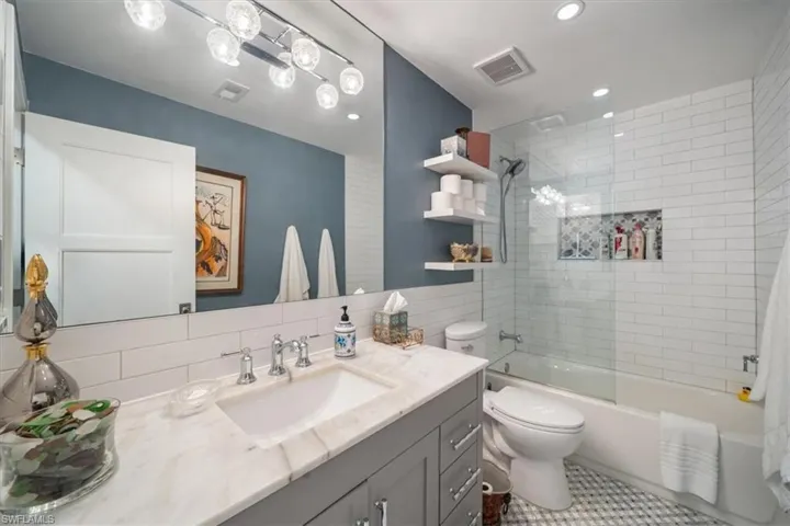 Full bathroom with tiled shower / bath, tile floors, tasteful backsplash, large vanity, and toilet