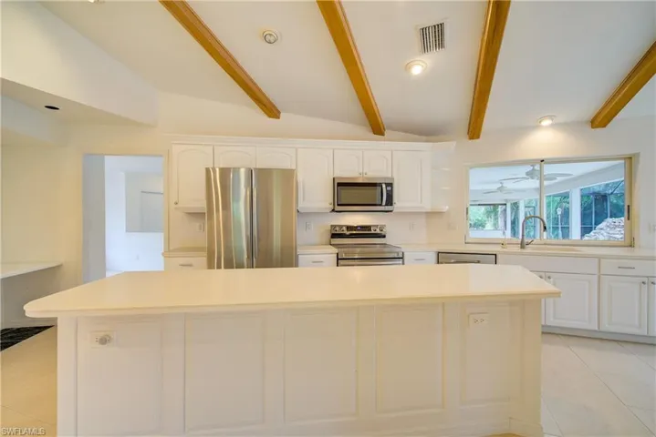 Kitchen with stainless steel appliances, vaulted ceiling with beams, a kitchen island, white cabinets, and sink