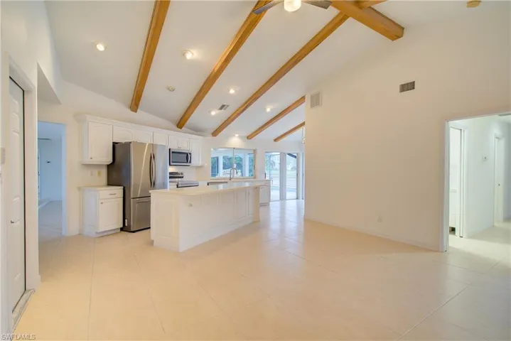 Kitchen featuring appliances with stainless steel finishes, light tile patterned flooring, high vaulted ceiling, white cabinets, and a center island