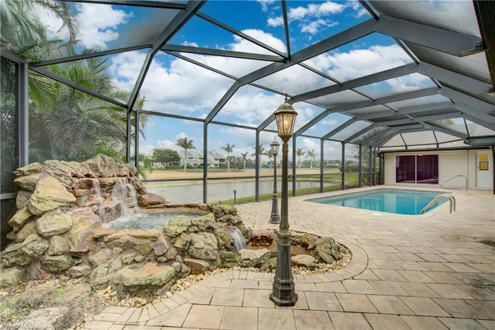 View of pool with pool water feature, a water view, a patio, and glass enclosure