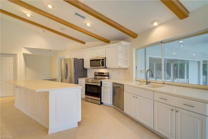 Kitchen with appliances with stainless steel finishes, vaulted ceiling with beams, a kitchen island, white cabinets, and sink