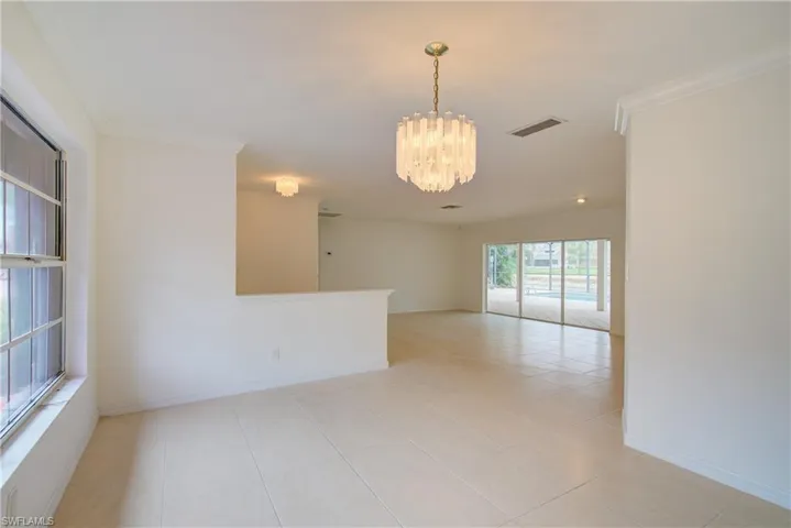 Tiled empty room featuring crown molding and a notable chandelier