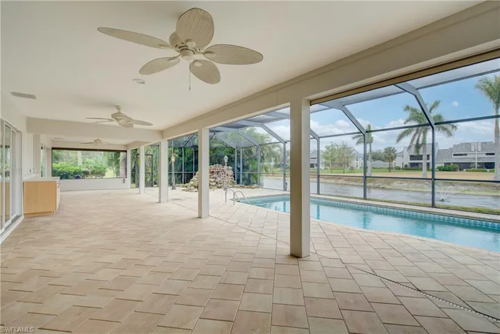 View of swimming pool with glass enclosure, ceiling fan, a water view, and a patio