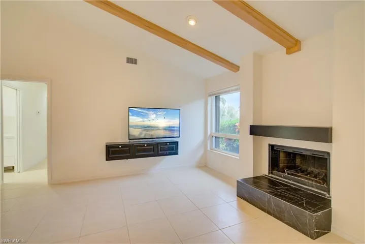 Tiled living room featuring lofted ceiling with beams and a tiled fireplace