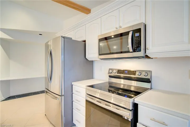 Kitchen featuring light tile patterned floors, white cabinets, appliances with stainless steel finishes, and vaulted ceiling with beams