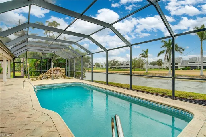 View of pool featuring glass enclosure, a water view, and a patio