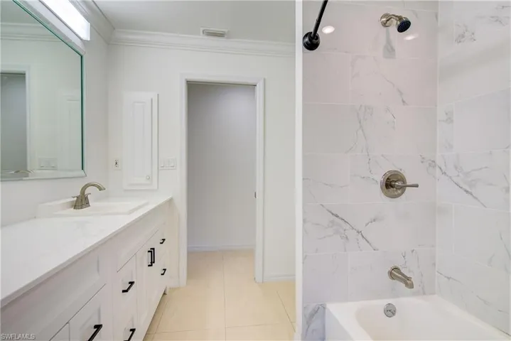 Bathroom with tiled shower / bath combo, tile patterned floors, vanity, and crown molding