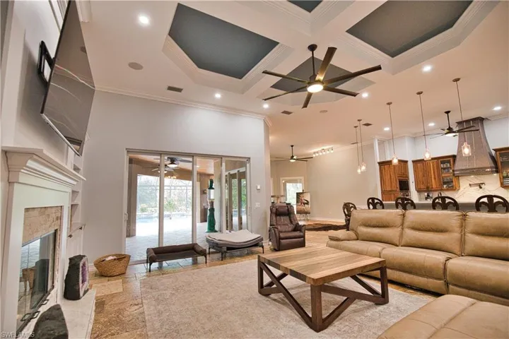 Tiled living room featuring ceiling fan, a high ceiling, crown molding, coffered ceiling, and a premium fireplace