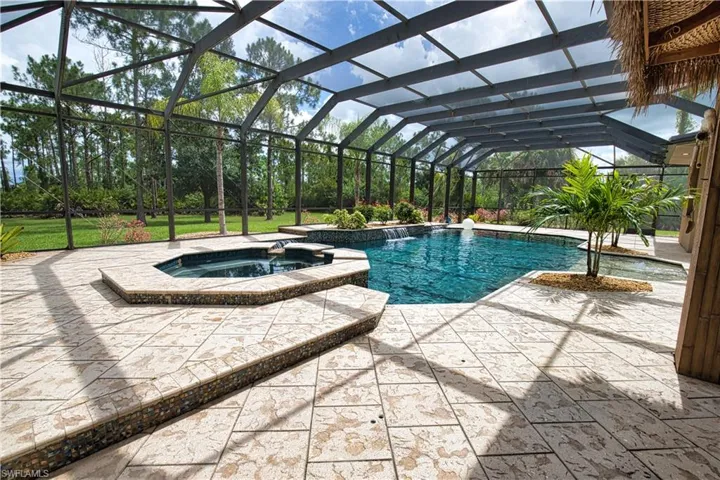 View of swimming pool with an in ground hot tub, a patio, pool water feature, and glass enclosure