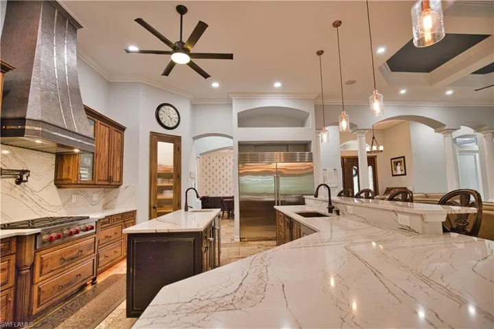 Kitchen with sink, pendant lighting, custom exhaust hood, ceiling fan, and a large island with sink
