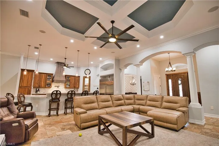 Tiled living room with coffered ceiling, ornate columns, ceiling fan with notable chandelier, and a high ceiling