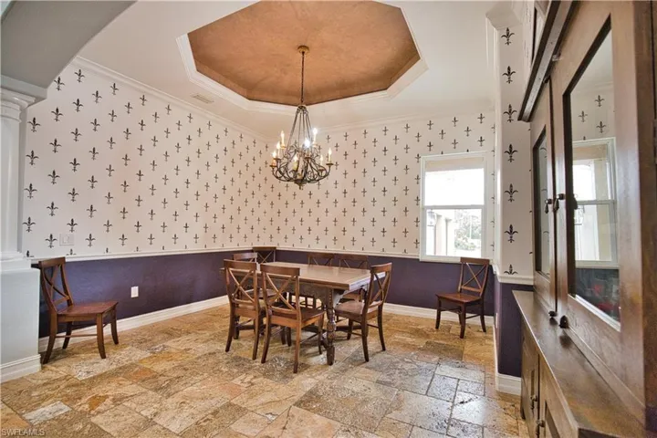 Tiled dining area featuring ornamental molding, decorative columns, a raised ceiling, and a chandelier