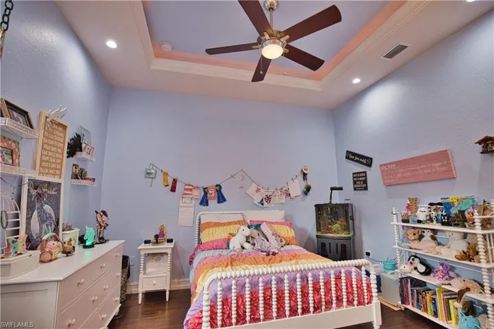 Bedroom featuring dark wood-type flooring, a raised ceiling, crown molding, and ceiling fan