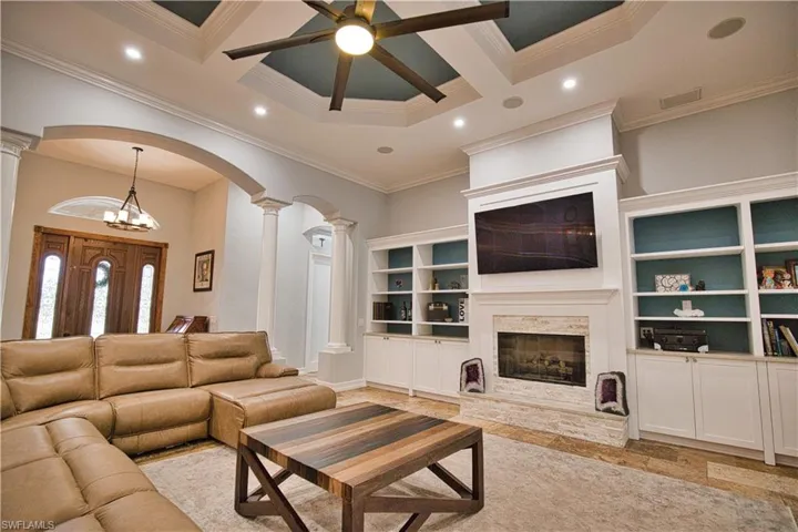 Living room featuring coffered ceiling, decorative columns, and a fireplace