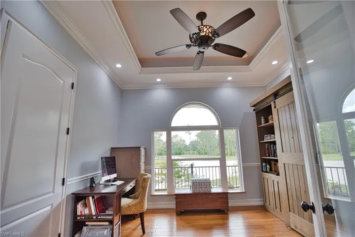 Home office with light hardwood / wood-style floors, a barn door, ceiling fan, and a raised ceiling