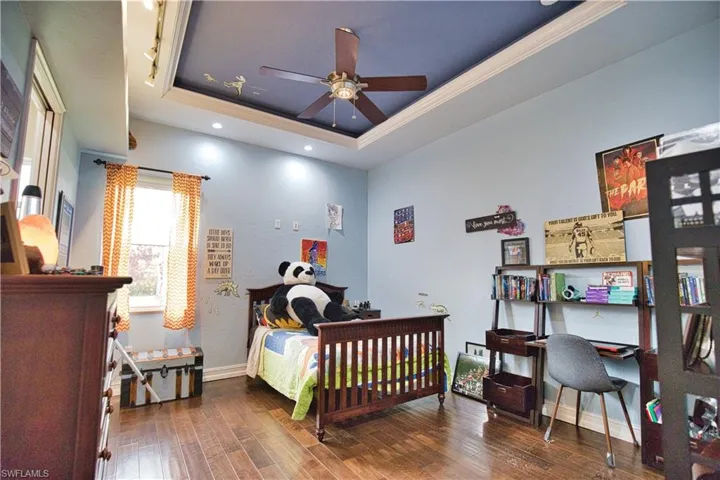 Bedroom featuring dark hardwood / wood-style flooring, ceiling fan, crown molding, and a tray ceiling