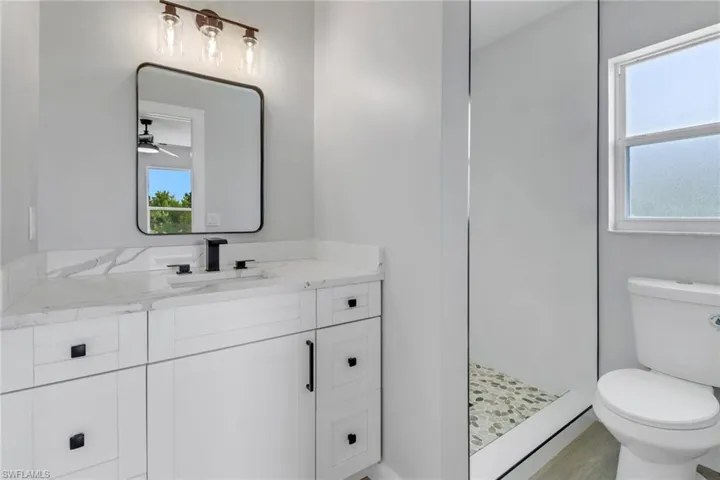 Bathroom featuring ceiling fan, toilet, walk in shower, and vanity