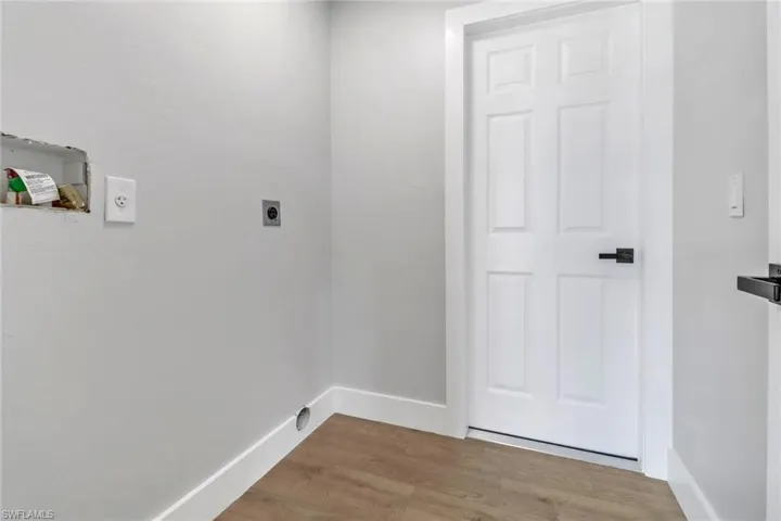 Clothes washing area with electric dryer hookup and light wood-type flooring