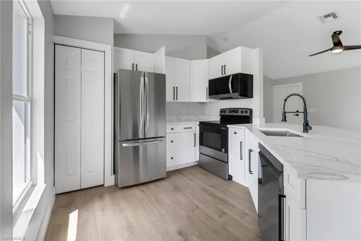 Kitchen featuring light wood-type flooring, vaulted ceiling, light stone counters, appliances with stainless steel finishes, and white cabinets