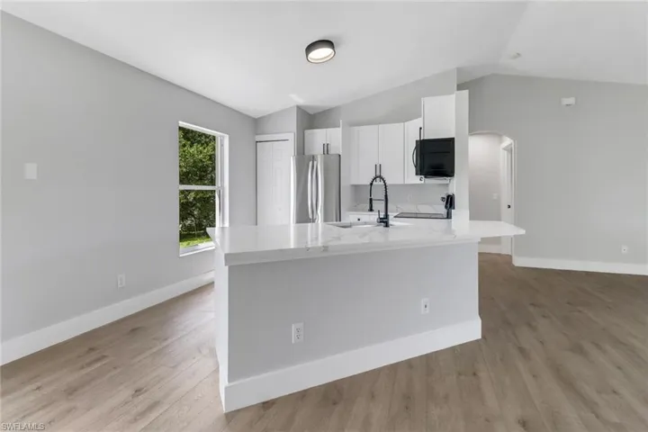 Kitchen featuring white cabinets, stainless steel fridge, light hardwood / wood-style floors, and vaulted ceiling