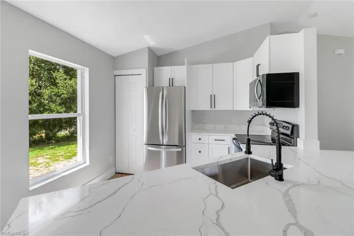Kitchen with appliances with stainless steel finishes, a wealth of natural light, and light stone counters