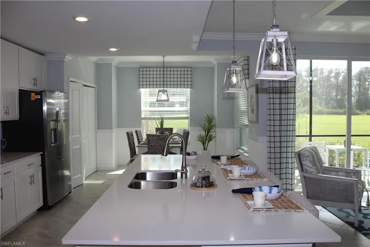 Kitchen with a sink, ornamental molding, a kitchen island with sink, stainless steel fridge with ice dispenser, and light countertops
