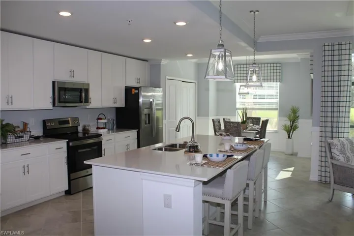 Kitchen featuring stainless steel appliances, a sink, ornamental molding, a kitchen island with sink, and light tile patterned floors