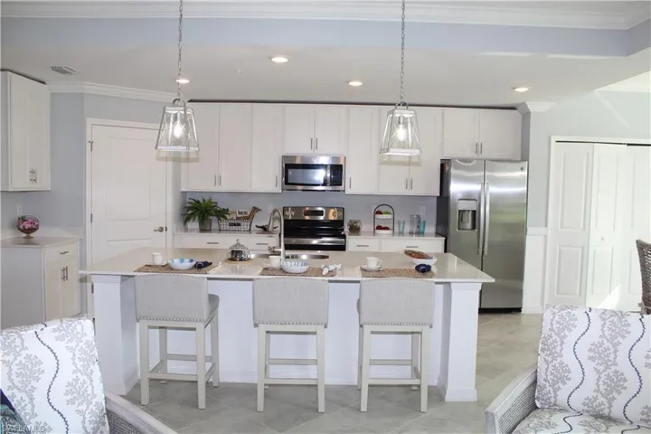 Kitchen featuring appliances with stainless steel finishes, a sink, ornamental molding, light countertops, and decorative light fixtures