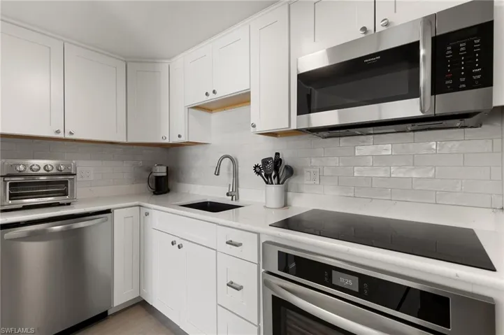 Kitchen with a toaster, stainless steel appliances, backsplash, white cabinetry, and a sink