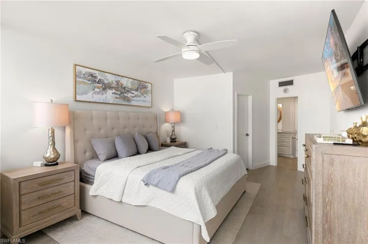 Bedroom with light wood finished floors, visible vents, baseboards, ceiling fan, and ensuite bathroom