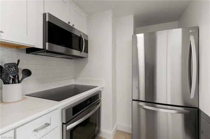 Kitchen featuring light stone counters, stainless steel appliances, baseboards, white cabinets, and backsplash