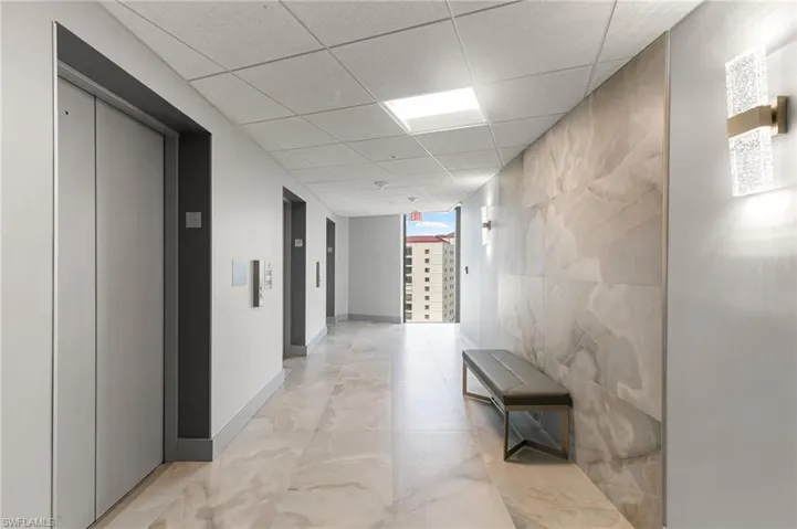 Hallway featuring a paneled ceiling, elevator, and baseboards