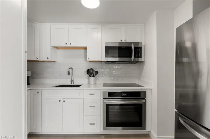 Kitchen featuring stainless steel appliances, light countertops, decorative backsplash, white cabinets, and a sink