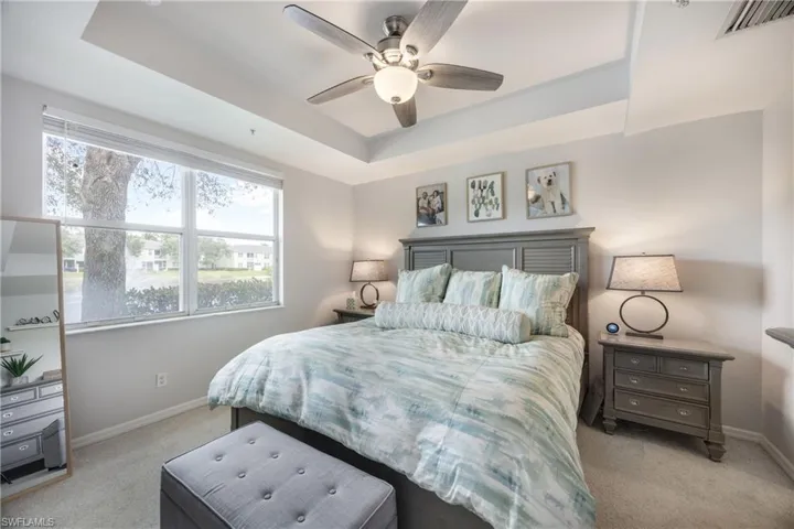 Bedroom with a tray ceiling, light colored carpet, and a ceiling fan