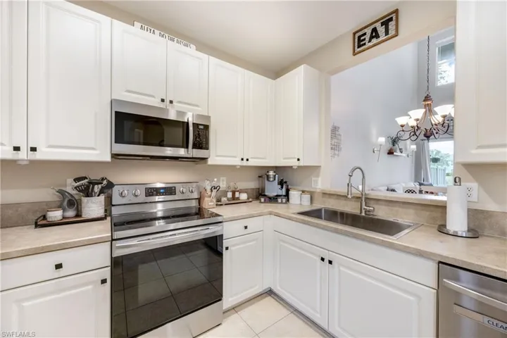Kitchen with appliances with stainless steel finishes, a chandelier, white cabinets, light tile patterned floors, and hanging light fixtures