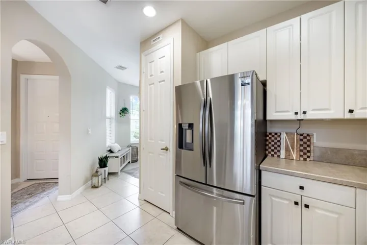 Kitchen featuring stainless steel refrigerator with ice dispenser, light countertops, arched walkways, white cabinetry, and light tile patterned floors