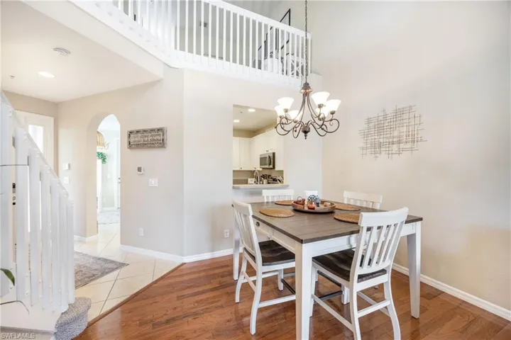 Dining space featuring light wood-style flooring, a towering ceiling, arched walkways, stairs, and a chandelier