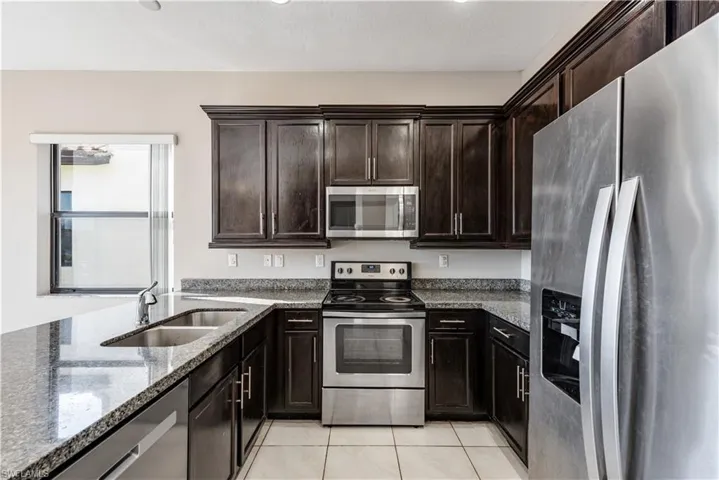 Kitchen with light tile patterned flooring, stone countertops, stainless steel appliances, dark brown cabinetry, and sink