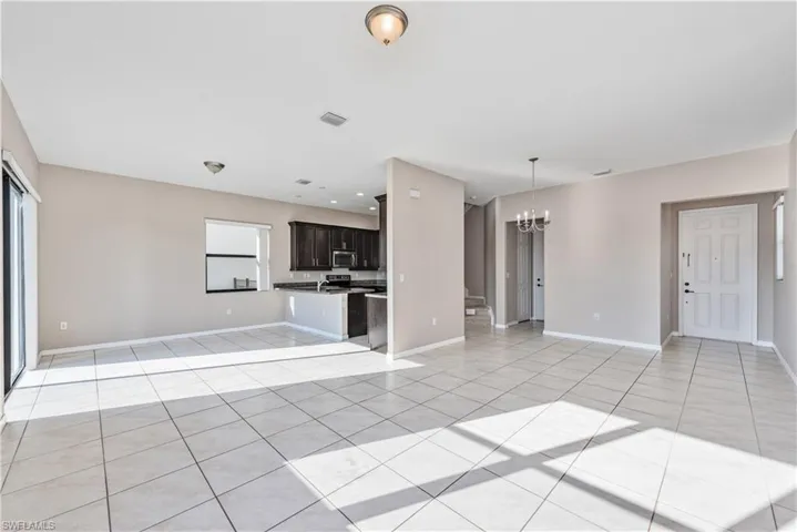Unfurnished living room featuring plenty of natural light, light tile patterned floors, and a notable chandelier